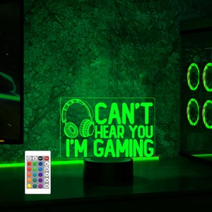 May include: A green LED night light with a remote control. The light features a graphic of headphones and the text "Can't hear you I'm gaming".