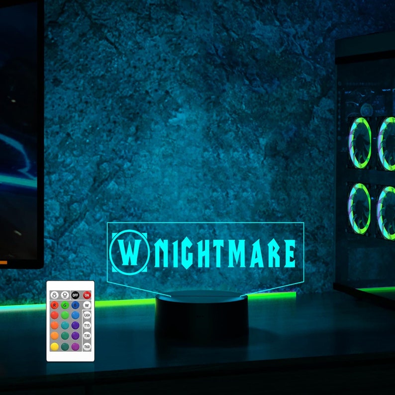 May include: A blue and green LED light with a black base. The light features a white "W" logo and the text "NIGHTMARE". The light is on a dark surface with a remote control in the foreground.