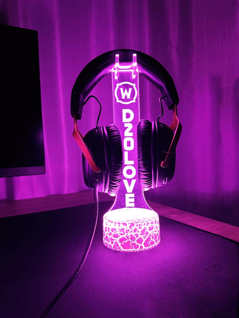 Op de afbeelding: Een paarse LED-lichtstandaard met een wit logo met de tekst "W D2OLOVE" en een zwarte koptelefoon op de standaard.