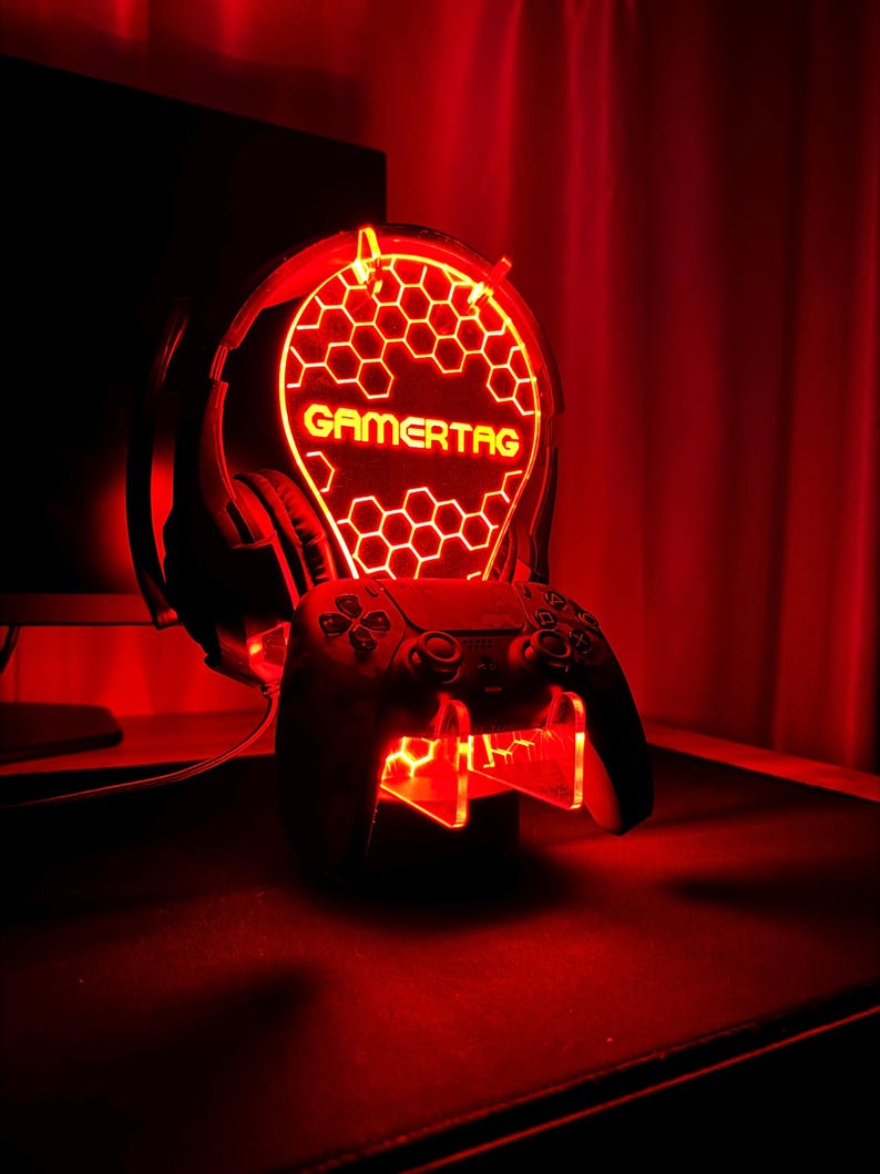 May include: A red illuminated gaming headset stand with a honeycomb design and the word "GAMERTAG" in yellow. The stand also includes a slot for a video game controller.