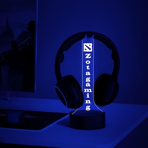 May include: A white LED lamp with the word "Zotac Gaming" written vertically on the front. The lamp is on a desk next to a pair of black headphones.