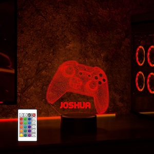 May include: A red illuminated 3D printed gamer controller night light with the name Joshua printed below it. The light is on a black base and is controlled by a remote with multiple color options.