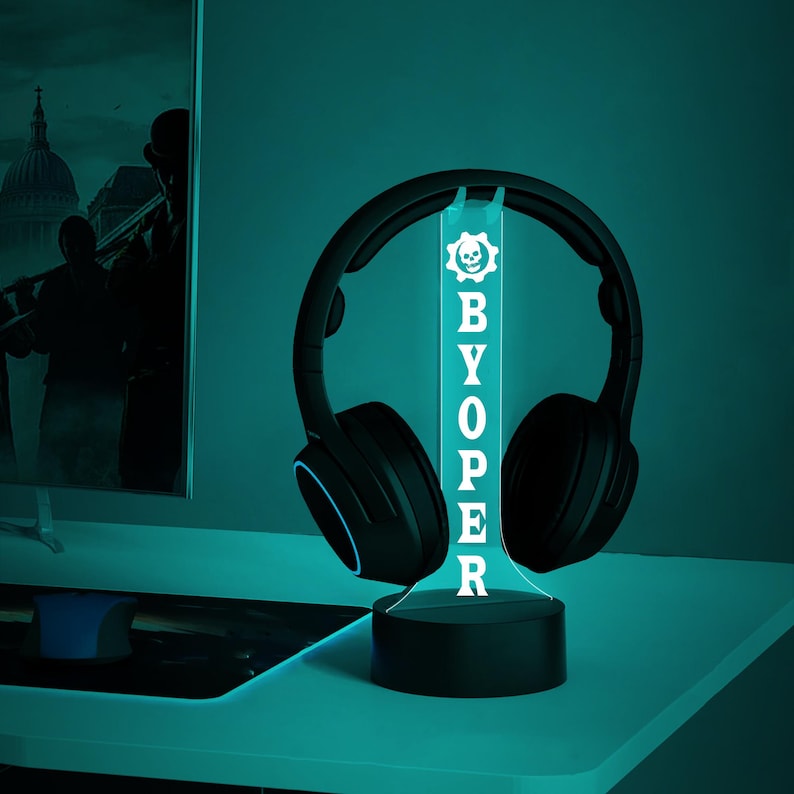 Op de afbeelding: Een zwarte en blauwe gaming headset standaard met een schedel afbeelding en de tekst "BYOPER" in wit. De standaard is verlicht met blauw licht.