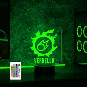 May include: A green and white LED night light with a stylised flame design and the name "VERNELLA" printed below. The light is on a black base and has a remote control with multiple colour options.
