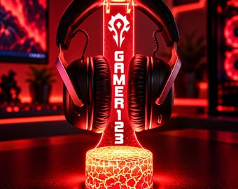 Könnte beinhalten: Ein schwarzes Headset ruht auf einem vertikalen, beleuchteten roten Acrylständer. Der Ständer zeigt ein weißes Horde-Fraktionssymbol über dem vertikalen Text GAMER123. Der Sockel hat eine leuchtende, rissige Lava-Textur in Rot und Orange.