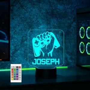 Könnte beinhalten: Ein blaues und weißes personalisiertes LED-Nachtlicht mit einem Gamer, der einen Videospiel-Controller hält. Der Name "JOSEPH" wird auf dem Licht angezeigt.
