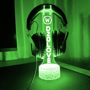 Op de afbeelding: Een groene LED-lichtstandaard met een transparant acryl paneel waarop "W D2OLOVE" staat en die een zwarte koptelefoon vasthoudt.