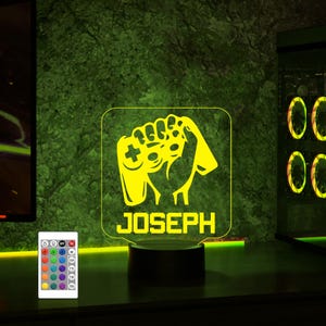May include: A yellow LED night light with a gamer hand holding a video game controller. The light has a personalized name "JOSEPH" on the bottom. The light is on a black base and comes with a remote control.