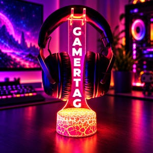 May include: A black over-ear headset rests on a clear acrylic stand featuring the vertical text GAMERTAG. The stand has a circular base with a glowing, cracked-texture pattern illuminated in vibrant red and orange light.