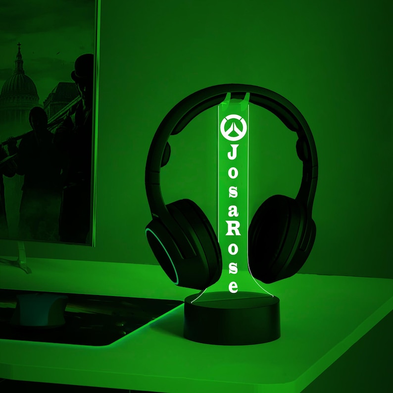 May include: A green LED light with a black base and a black headset resting on it. The light has the Overwatch logo and the name "JosaRose" printed on it.