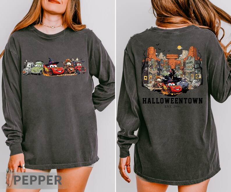 K&ouml;nnte beinhalten: Dunkelgraues Langarmshirt mit einem Halloween-Motiv von animierten Autos auf der Vorderseite. Die R&uuml;ckseite des Shirts zeigt eine detaillierte Illustration einer Stadt mit dem Text "Halloweentown" und "Est. 2003".