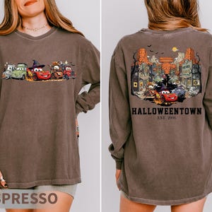 K&ouml;nnte beinhalten: Lang&auml;rmliges Espresso-farbenes T-Shirt mit einem Cartoon-Auto-Motiv auf der Vorderseite und einer detaillierten Illustration einer Stadt mit dem Text "Halloweentown Est. 2006" auf der R&uuml;ckseite. Das Shirt hat eine lockere Passform.