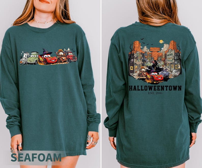 K&ouml;nnte beinhalten: Seegr&uuml;nes Langarm-Sweatshirt mit einem Halloween-Motiv von animierten Autos auf der Vorderseite. Auf der R&uuml;ckseite des Sweatshirts befindet sich eine detaillierte Illustration einer gruseligen Stadt mit dem Text "Halloweentown Est. 2006".