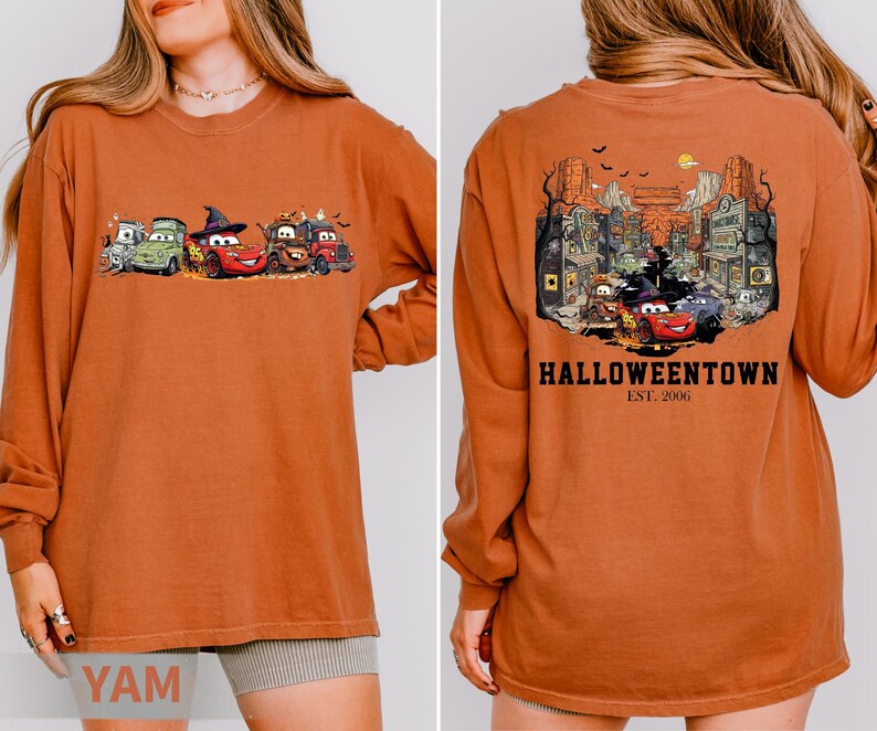 K&ouml;nnte beinhalten: Gebrannt orangefarbenes Langarmshirt mit einem Halloween-Motiv von animierten Autos. Auf der Vorderseite sind Autos in Kost&uuml;men zu sehen, w&auml;hrend die R&uuml;ckseite eine gruselige Stadtszene mit dem Text "Halloweentown Est. 2006" zeigt.