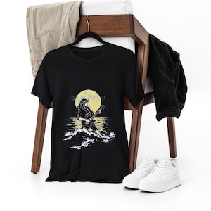 May include: Black t-shirt with a graphic of a person playing a guitar in front of a yellow moon and waves. The text "G 01" is on the shirt.
