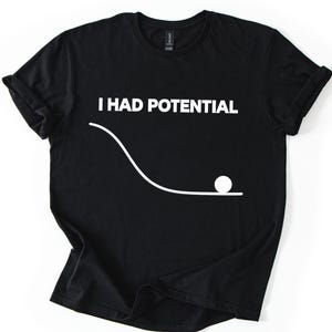 May include: Black t-shirt with the white text "I HAD POTENTIAL" above a white line drawing of a ball rolling down a curved path. The shirt has short sleeves and a crew neck.