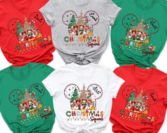 May include: A collection of five short-sleeve t-shirts in red, gray, green, and white. Each shirt features a graphic of Mickey Mouse ears containing a castle, Christmas trees, and Disney characters with the text Christmas Squad.