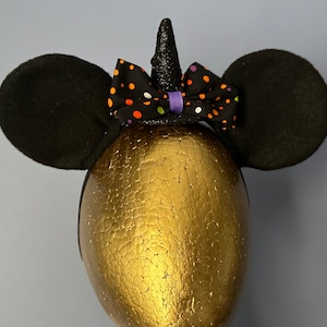 May include: Black mouse ears headband with a purple and orange polka dot bow and a sparkly black unicorn horn.