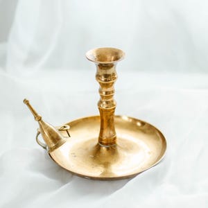 Peut inclure: Un bougeoir en métal doré avec une base ronde et un seul porte-bougie. Le bougeoir a un petit bec verseur sur le côté.