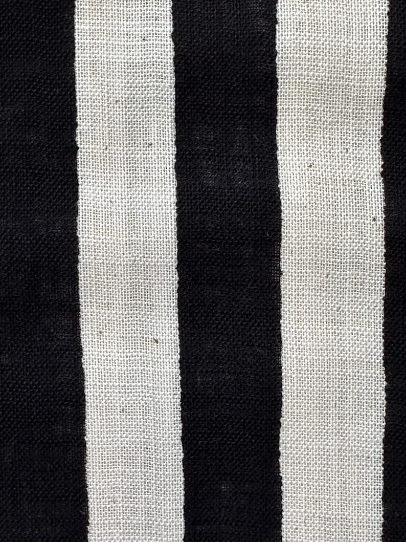 May include: A textile fabric featuring a repeating pattern of vertical stripes in solid black and off-white. The material displays a visible woven texture with a consistent weave density throughout, creating a high-contrast linear design.