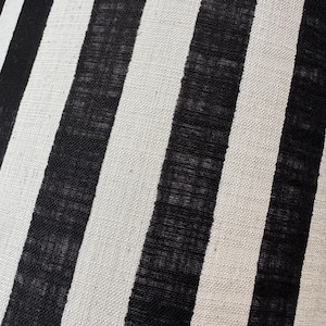May include: A textile fabric featuring a repeating pattern of vertical stripes in alternating black and off-white colors. The material has a visible woven texture with a consistent weave throughout, creating a high-contrast linear design.