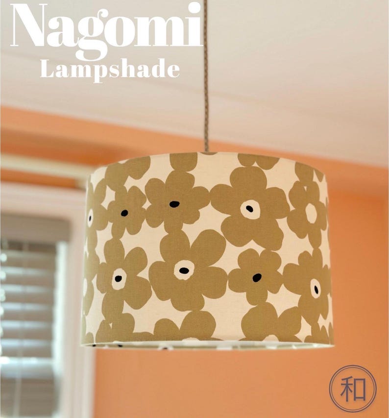 May include: A cylindrical lampshade featuring a repeating pattern of large, olive-green flowers with dark centers on a cream background. The text Nagomi Lampshade is visible at the top, and a circular logo with the Japanese character 和 is at the bottom.
