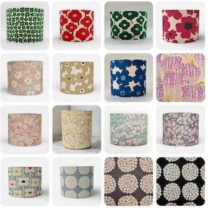 May include: A selection of cylindrical lampshades showcasing diverse floral designs. Patterns include red poppies, green and white flowers, and blue blooms. Other shades feature delicate blossoms in pink, beige, and lavender, and a grey and white floral pattern.