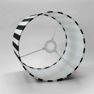 May include: A cylindrical lamp shade featuring a bold black and white striped pattern. The interior structure consists of a white metal frame with three spokes connecting to a central ring fitting, designed for attachment to a lamp base socket.