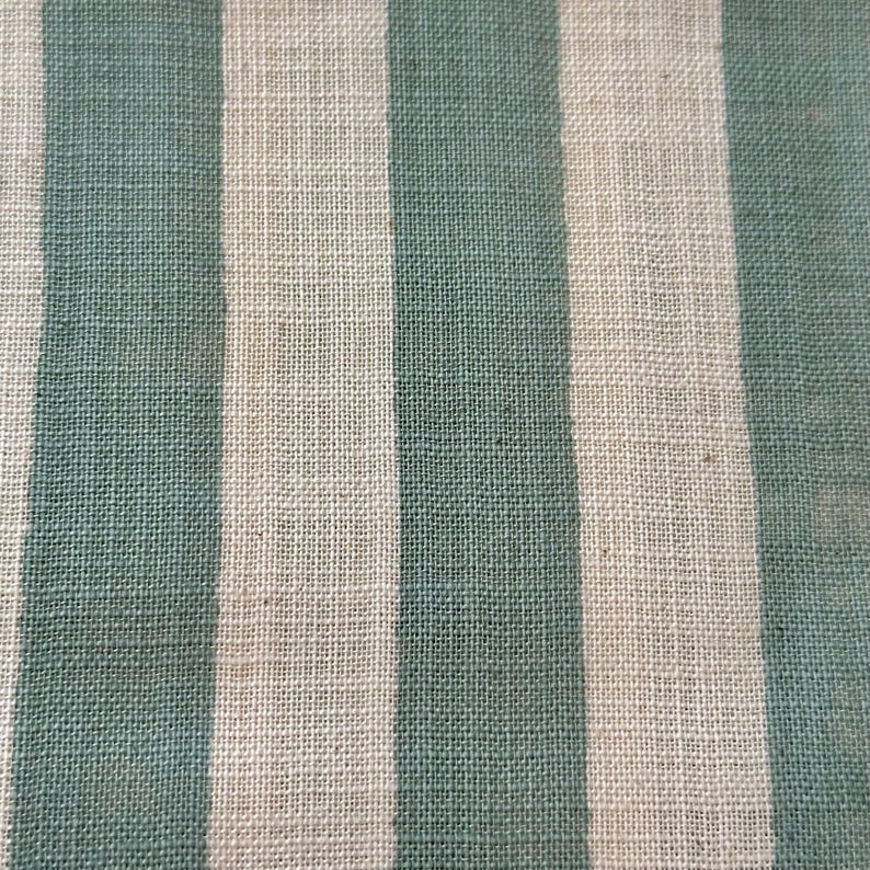 May include: A woven fabric featuring a repeating pattern of vertical stripes in alternating shades of muted sage green and off-white. The textile displays a visible, textured weave with a consistent grid-like structure throughout the entire surface.