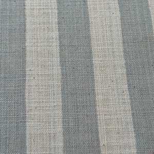 May include: A woven fabric featuring a repeating pattern of vertical stripes in alternating shades of muted slate blue and off-white. The textile displays a visible, textured grid-like weave structure throughout the entire surface of the material.
