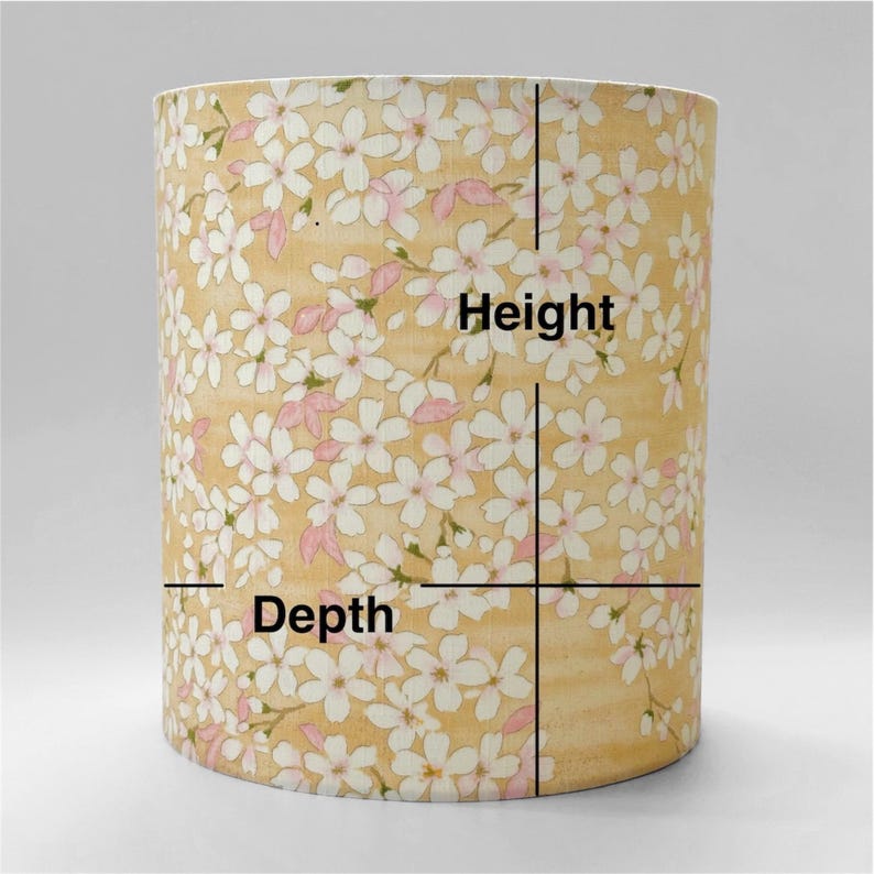 May include: A cylindrical lampshade featuring a light yellow background with a repeating pattern of white and pale pink cherry blossom flowers. Black lines are overlaid on the surface with the text Height and Depth indicating dimensions.