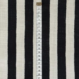 May include: A fabric featuring a pattern of vertical black and off-white stripes. A white measuring tape is placed vertically over the fabric, showing markings from 2 to 21 inches, with the text Made in Germany printed near the top edge.