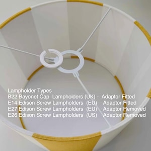 May include: A drum lampshade featuring alternating vertical stripes of white and mustard yellow. The interior includes a white metal spider fitter with a removable adaptor. Text lists compatibility: B22, E14, E27, and E26 lampholder types.