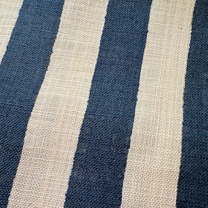 May include: A textile fabric featuring a repeating pattern of vertical stripes in deep navy blue and off-white. The material has a visible, coarse, woven texture with a consistent grid-like structure throughout the entire surface of the cloth.