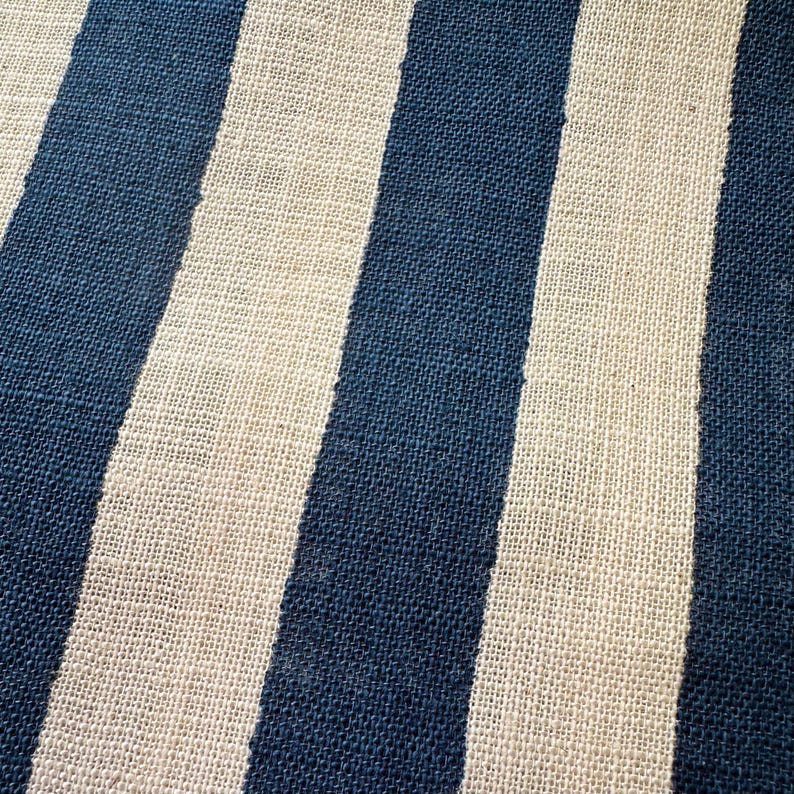 May include: A textile fabric featuring a repeating pattern of vertical stripes in deep navy blue and off-white. The material has a visible, coarse, woven texture with a consistent grid-like structure throughout the entire surface of the cloth.