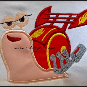 May include: Embroidered patch of a red snail with a yellow and red racing car shell. The snail has a pink body, red lips, and brown eyes with eyelashes. The text "www.cutebykira.com" is embroidered on the snail's shell.