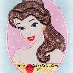 May include: Embroidered patch of Belle from Beauty and the Beast. She has brown hair, a yellow dress, and a red rose. The patch is in an oval shape with a pink background and white polka dots. The text "www.cutebykira.com" is at the bottom of the patch.