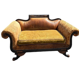 May include: An antique loveseat with a dark brown wooden frame and ornate detailing. The seat cushion is a golden yellow, and the back and arms are a textured brown. The arms have a floral pattern. The loveseat has curved arms and legs.