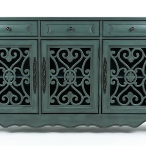 May include: A teal-colored wooden sideboard featuring three top drawers with small round knobs and three lower cabinet doors. Each door displays an intricate, open-work scroll pattern with a central floral motif and dark metal hardware.