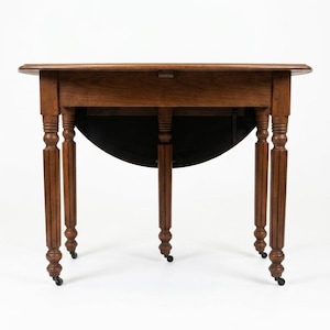 May include: A brown wooden drop-leaf table with a smooth rectangular top and rounded edges. The table features four turned, fluted legs, each equipped with a small black caster wheel at the base, and a hinged leaf mechanism underneath.