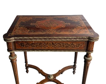 May include: A dark brown antique table with intricate inlaid wood designs and brass accents. The table has a rectangular top with rounded corners, a single drawer, and four ornate legs. The table measures approximately 30 inches long, 20 inches wide, and 28 inches high.