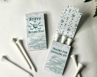 May include: Two rectangular paper matchbook-style holders with white and green golf-themed graphics. One holder is closed, reading "STEVE IS 70 Est. 1956 SEVEN-TEE!" The other is open, revealing white golf tees and the text "THANKS FOR SWINGING BY!"
