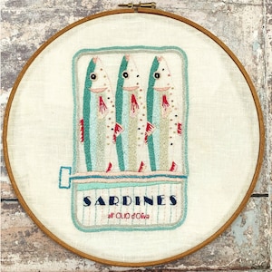 May include: Embroidered hoop art featuring three cartoon sardines in a can with the text "SARDINES au GOÛT D'OIVA" on a white background.