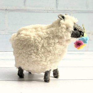 May include: A white fluffy sheep toy with a grey face holding a bouquet of colourful flowers. The flowers are pink, blue and yellow.