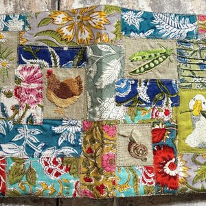 May include: A rectangular fabric panel featuring a patchwork of various floral and botanical prints in shades of blue, red, yellow, and green. Embroidered motifs include white daisies, a brown hen, green pea pods, a snail, and a white duck.