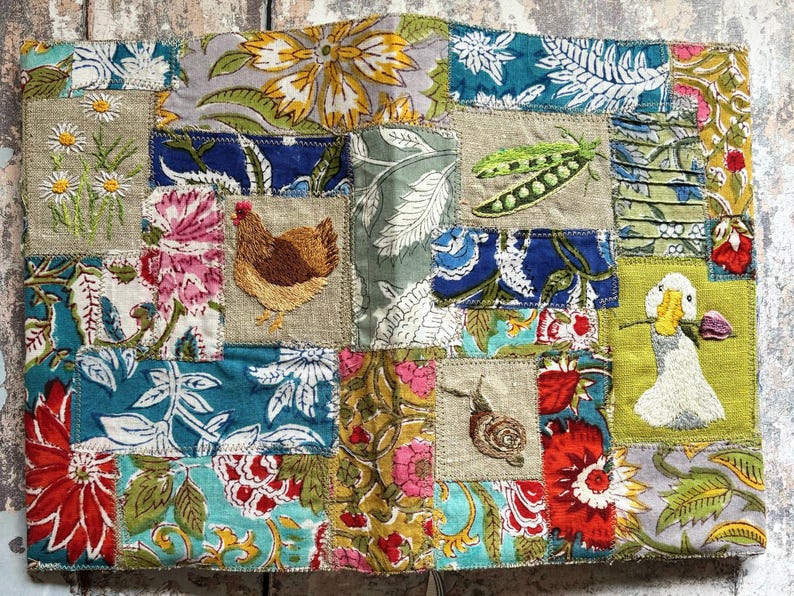 May include: A rectangular fabric panel featuring a patchwork of various floral and botanical prints in shades of blue, red, yellow, and green. Embroidered motifs include white daisies, a brown hen, green pea pods, a snail, and a white duck.