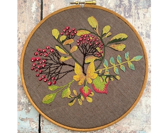 May include: Embroidered hoop art featuring a floral design with red berries, yellow and green leaves on a brown fabric background.