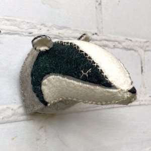 May include: A felt badger head wall hanging with black and white fur. The badger has a stitched black nose and white eyes.