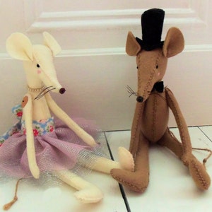May include: Two felt mouse dolls, one wearing a pink tutu and the other wearing a black top hat and bow tie.