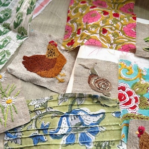 May include: A collection of fabric scraps featuring various patterns and embroidery. Pieces include a yellow floral print, a green and blue floral print, a brown embroidered chicken, a brown snail, and white daisies on linen.
